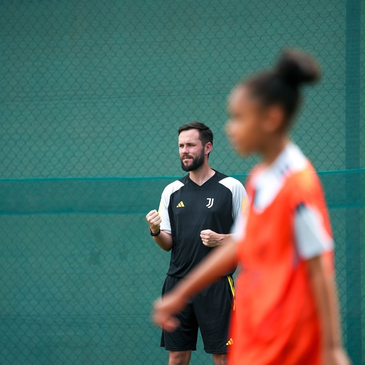 Dan Grimes watching a session closely, fists clenched, as a player runs past in the foreground