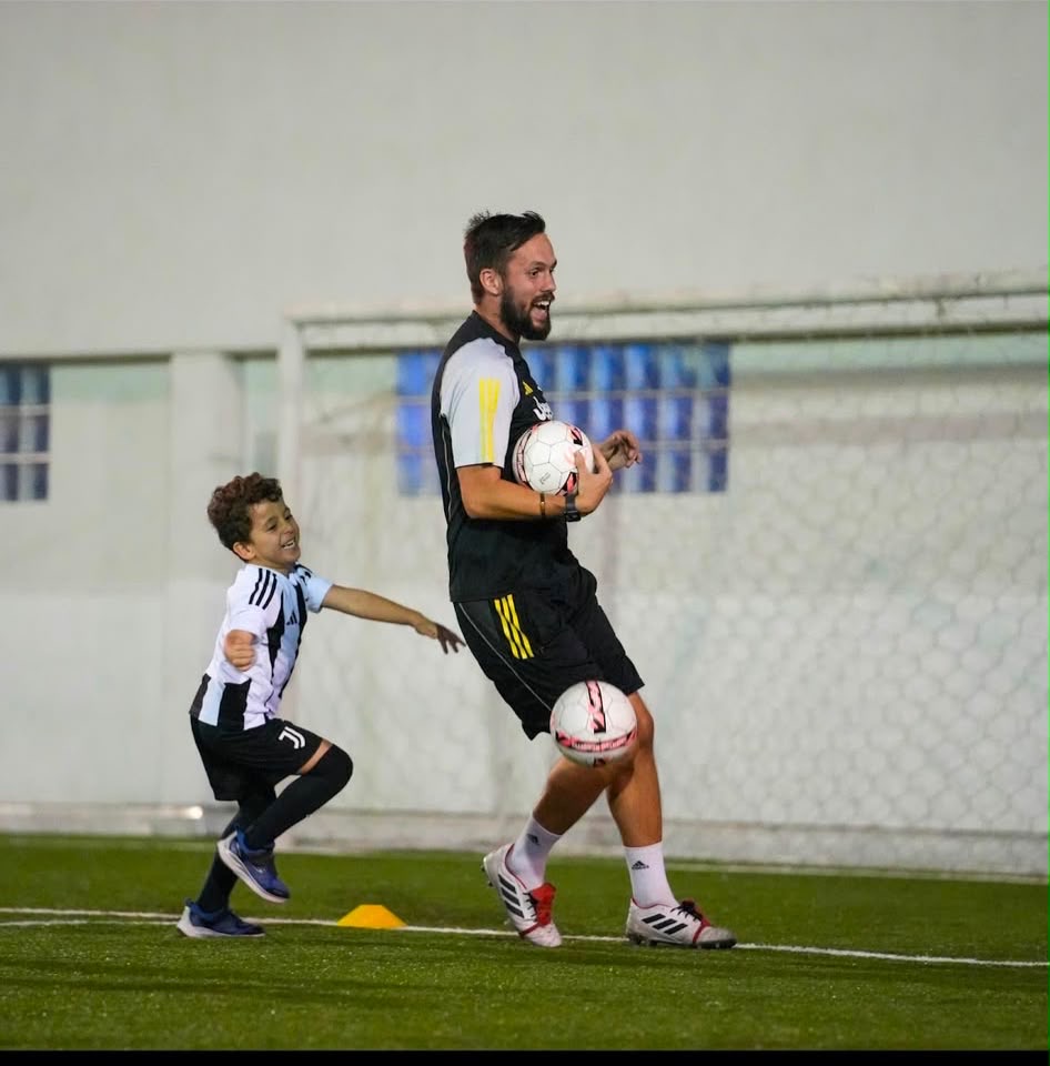 Dan Grimes laughing and playing with a young player during a Juventus Academy session